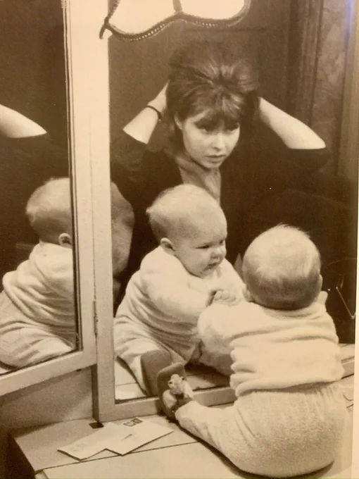 Pru sat at a dressing room mirror doing her hair, while a very young Sam is sat on the table facing the mirror.