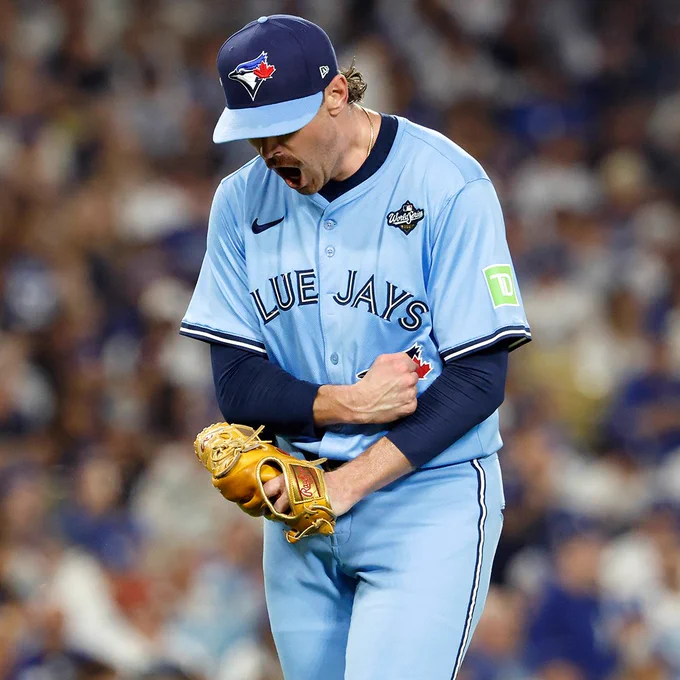 Shane Bieber shouts in celebration while walking off the mound. He is wearing a light blue Toronto Blue Jays jersey and a dark blue cap.