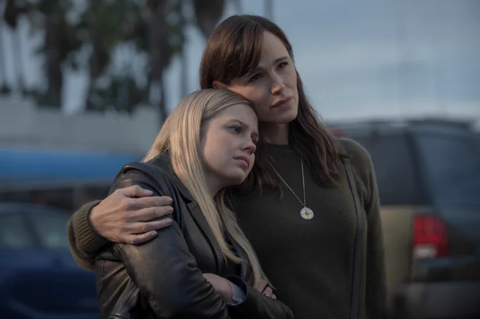 From The Last Thing He Told Me. Bailey Michaels portrayed by Angourie Rice and Hannah Hall portrayed by Jennifer Garner stand next to each other. Jennifer Garner has an arm wrapped around Angourie Rice while Angourie’s head leans on Jennifer’s shoulder.