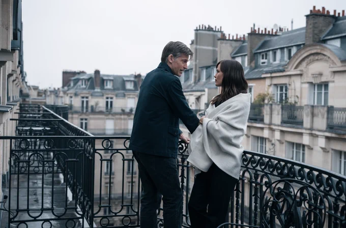 From The Last Thing He Told Me. Owen Michaels portrayed by Nikolaj Coster-Waldau stands on a balcony looking at Hannah Hall portrayed by Jennifer Garner.
