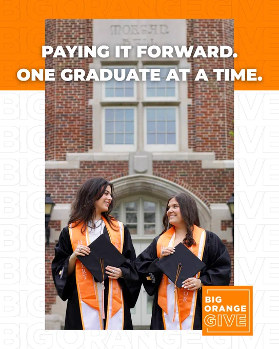 Two graduates in orange stoles and black caps stand in front of a brick building with "BIG ORANGE GIVE" and a university logo, smiling at each other. Text on the image reads "PAYING IT FORWARD. ONE GRADUATE AT A TIME."