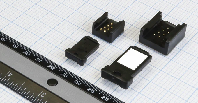 Electronic connectors and a small display screen alongside a metal ruler on a grid-patterned surface.