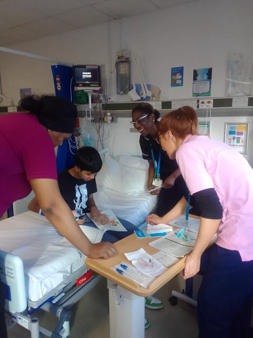 Healthcare workers in a hospital room engage with a child patient sitting on a bed. The patient is holding an activity book.