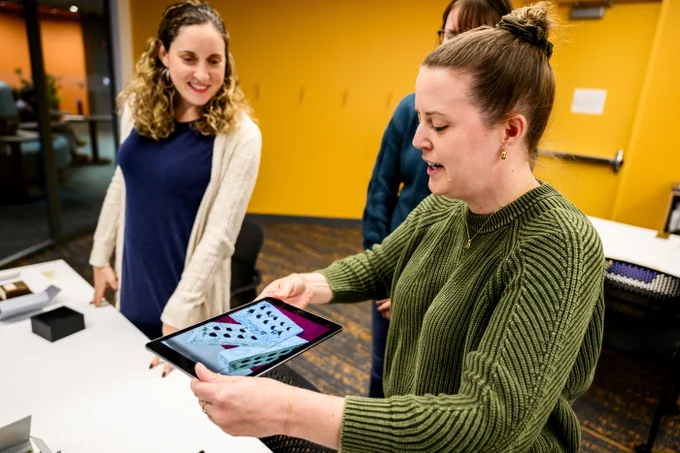 A person takes a photo of materials with an iPad while another looks on