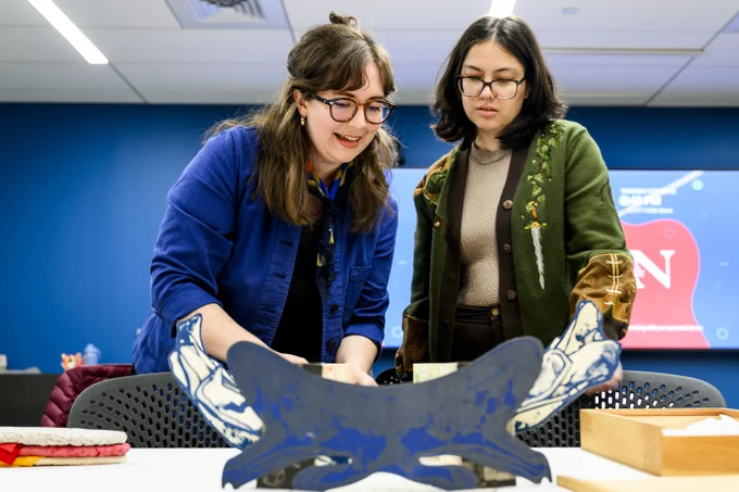 Two people stand at a table looking at a large blue and white unfolded document