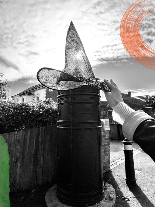 An electrical Lucy Box, photographed in black and white. A witches hat is held up in the photo, and green and orange elements have been added to the picture.