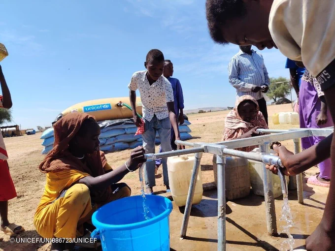 Children and families displaced collect water from a tap