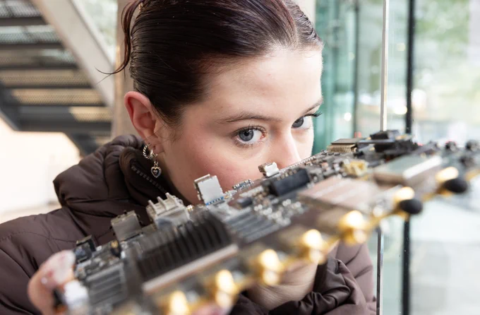 A person closely examining a complex electronic circuit board with focus and attention.
