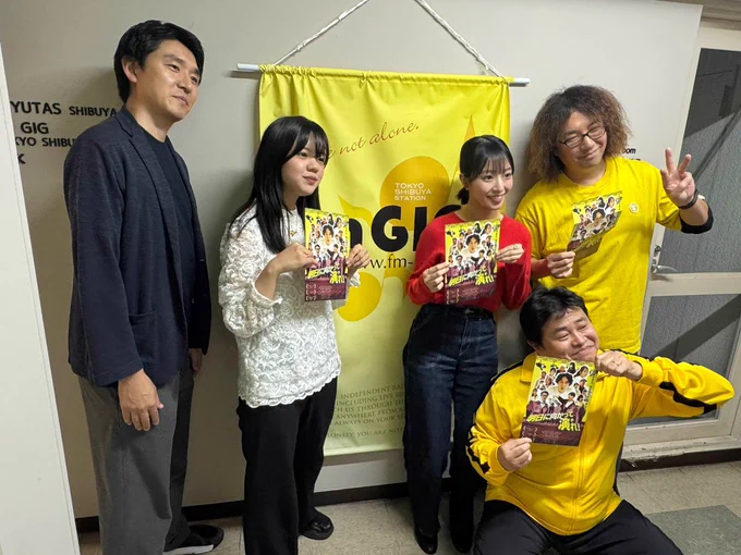 黄色いタペストリーの前での記念写真。
右からフカサワ テツヒロさん、ニシムラ テツヤさん、ノグチ チヒロ、クマクラ ヒメコ、ワシズ ショウゴ監督が並んでいる。