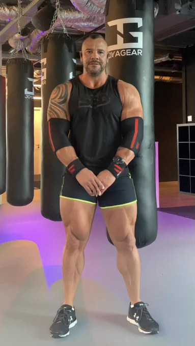 Muscular man in black athletic gear facing forward in the gym, exuding strength and dominance, ready for another round of training.