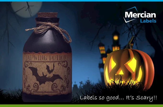 Picture of a bright Jack o Lantern / Carved Pumpkin in the foreground of a graveyard with an internally lit haunted mansion in the background on a dark night with a full, but shaded moon, with an old, short but stout glass bottle in the foreground with a label on it saying Bat Wing potion and text to the side saying ‘Labels so good… It’s scary!!’.