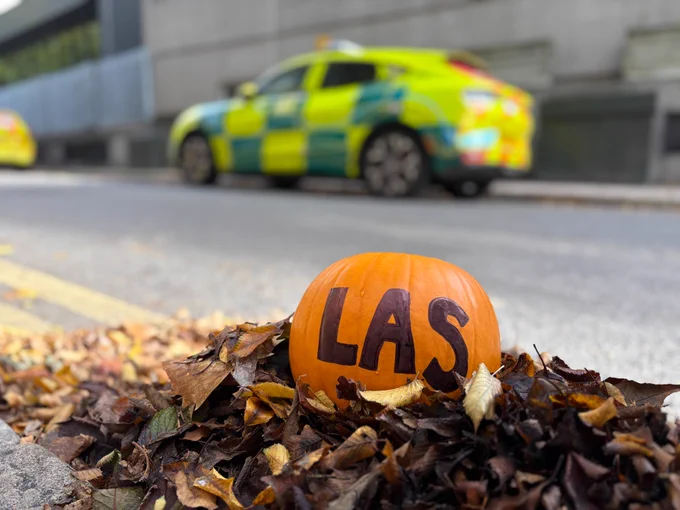 A Halloween pumpkin marked with 'LAS', in a bed of autumn leaves with an ambulance fast response car in the background. 