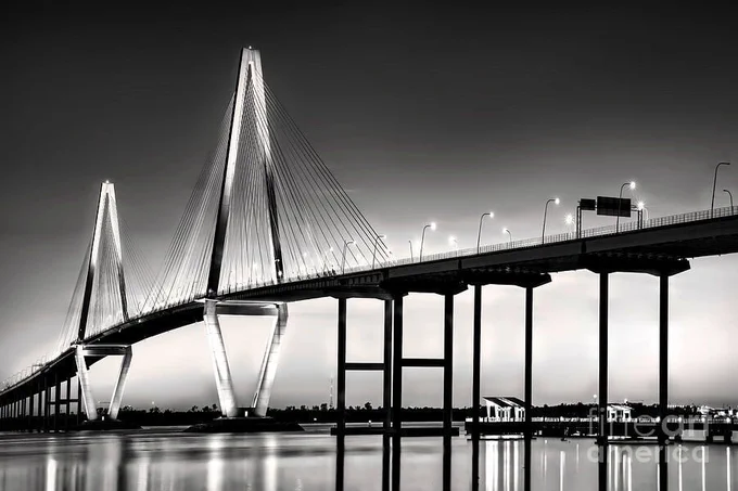 Black-and-white photograph of Arthur J. Ravenel Bridge in Charleston SC at night, with illuminated cables and shimmering water reflections. From the Fine Art Gallery of Shelia Hunt.
