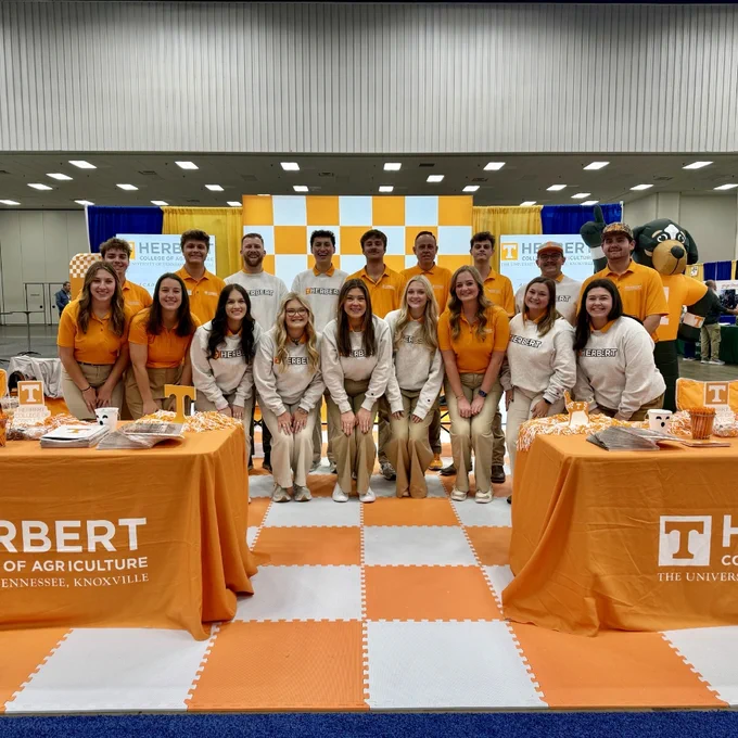 Group of University of Tennessee students standing in front of a promotional booth at an event, with mascot and banners featuring the university colors and logo.