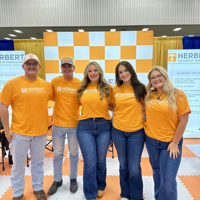 Five people wearing orange shirts standing in front of a University of Tennessee Herbert College of Agriculture promotional backdrop.