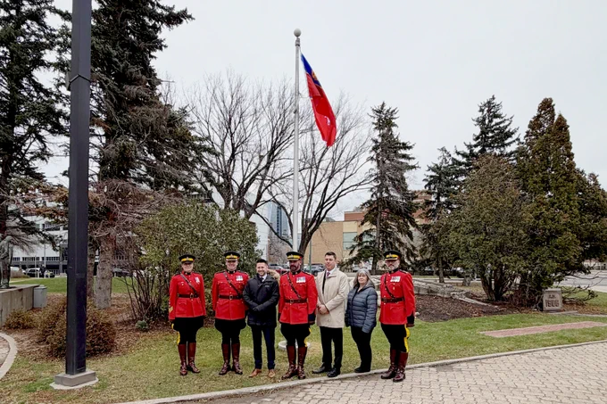 A group of mounties in red serge stand with provincial and municipal government officials at Regina City Hall. 