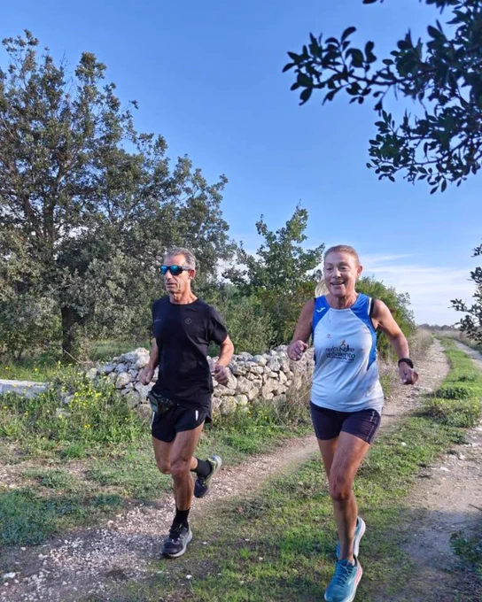 Two parkrunners in shorts running together on a grassy path.