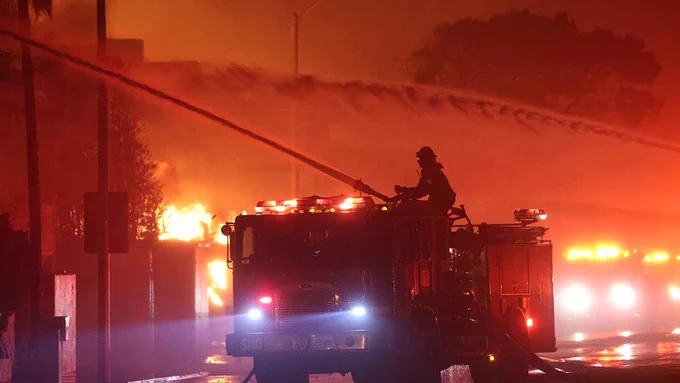 Firefighter on top of fire truck using hose to spray water on burning homes 