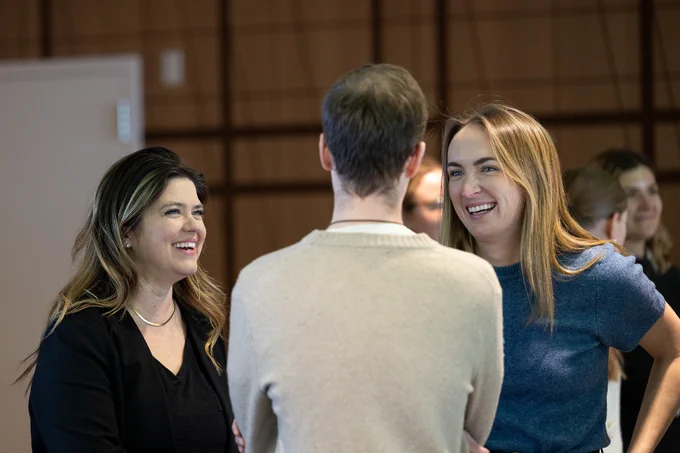 Two women smile while in conversation with a man who has his back to the camera