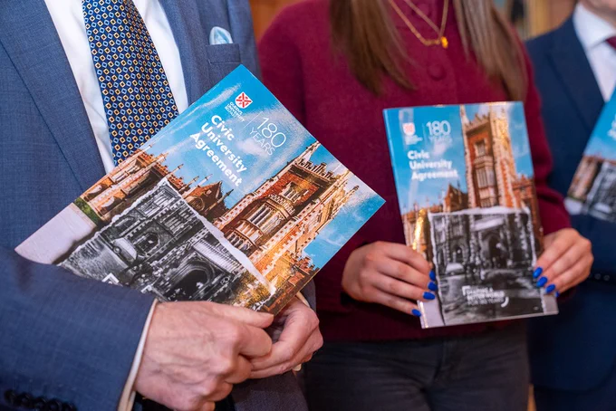 Image shows Professor Sir Ian Greer and a young person from RCity Belfast holding copies of the University's Civic Agreement.