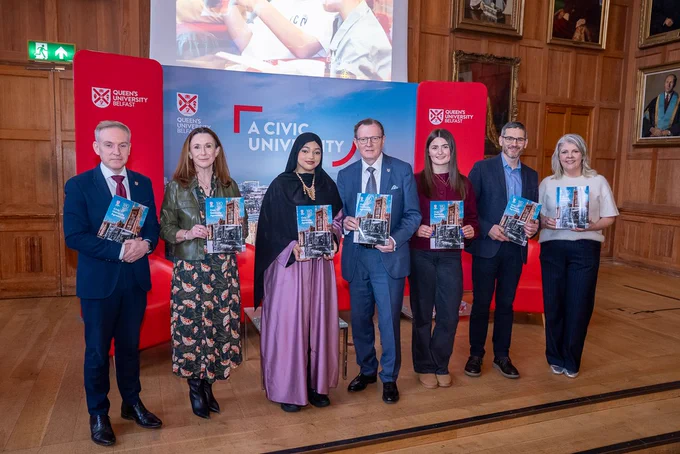 Image shows Queen's staff and community partners on stage in the Whitla Hall. They are all holding copies of the University's Civic Agreement.