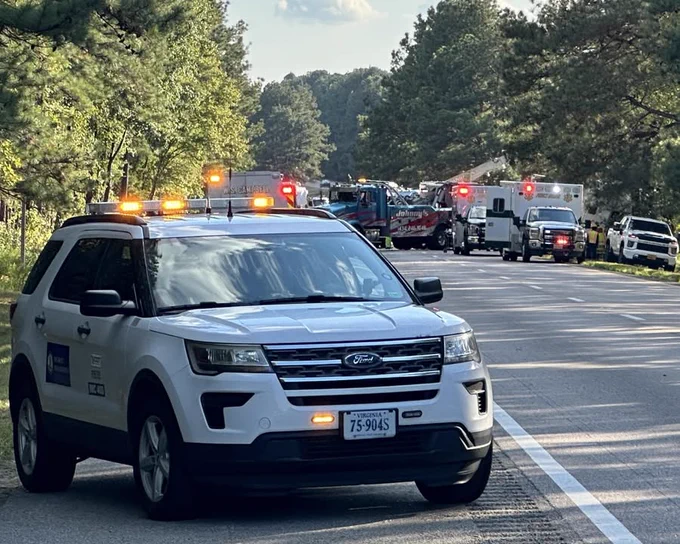 Emergency response scene with a VDOT Incident Response vehicle in the foreground and various emergency vehicles, including fire trucks and ambulances, in the background on a tree-lined Virginia interstate.