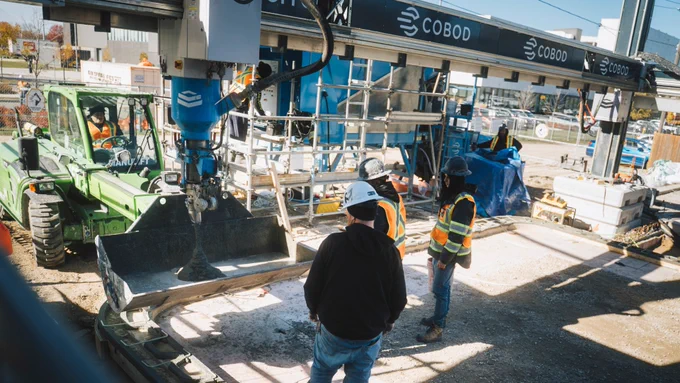 a person standing in front of 3D printer pouring concrete