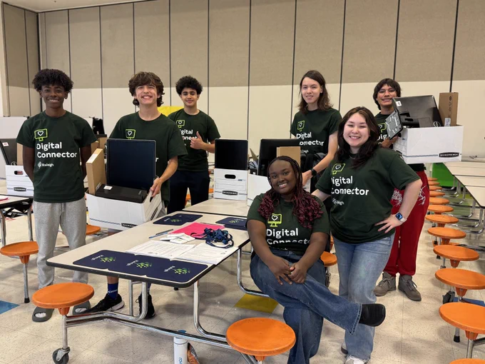 Seven students smile while holding computer equipment 