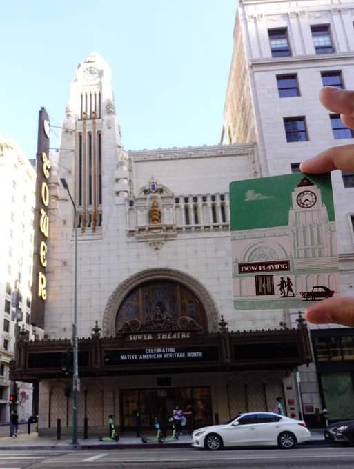 A playing card from the upcoming Downtown Las Palmas card game, being held in front of the Tower Theater on Broadway in downtown Los Angeles. The design on the card is a building with similar features to the theatre behind it.
