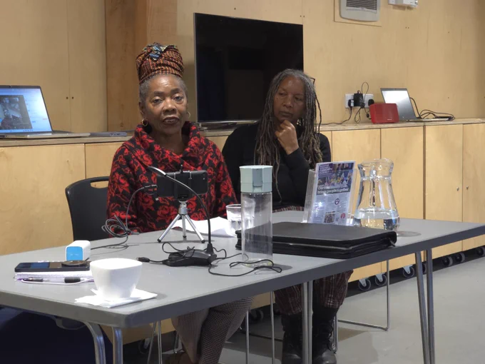 Sonia Winifred sat at a desk giving her presentation,  wearing a red coat
Amanda Onwuemene sat to sonias right wearing black
