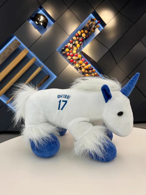 A white stuffed unicorn with blue horn and hooves. It has a white mane and “Ohtani 17” on its side in blue