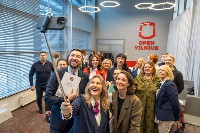 Group of people that were present during the signing of the Memorandum of Understanding (MoU) between Vilnius City and Cambridge International Education, posing for a selfie in a room with a banner reading "Open Vilnius" in the background.