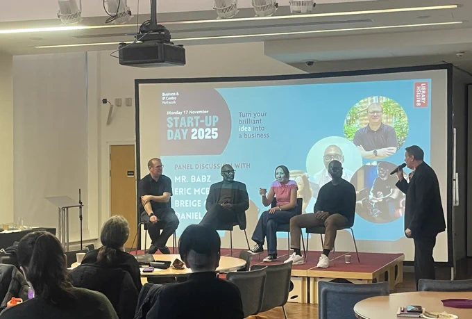 Panel of 4 sat in front of presentation screen being introduced by Jonathan Ebbs.