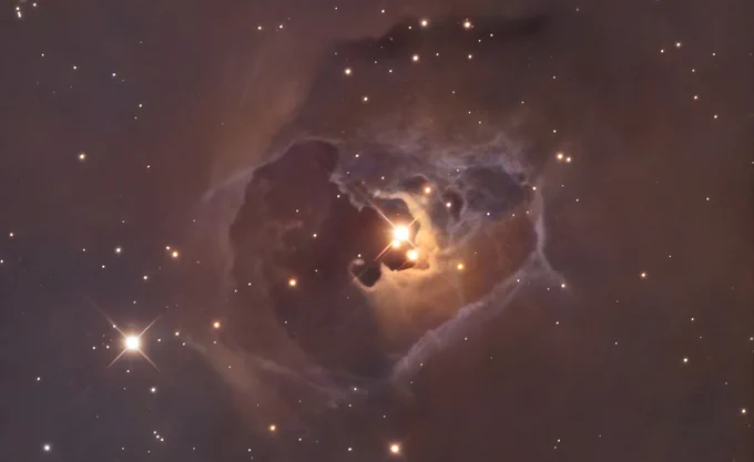 A luminous nebula in space with a glowing center, surrounded by wispy clouds of dust and gas. Bright stars are scattered across the dark, ethereal background.