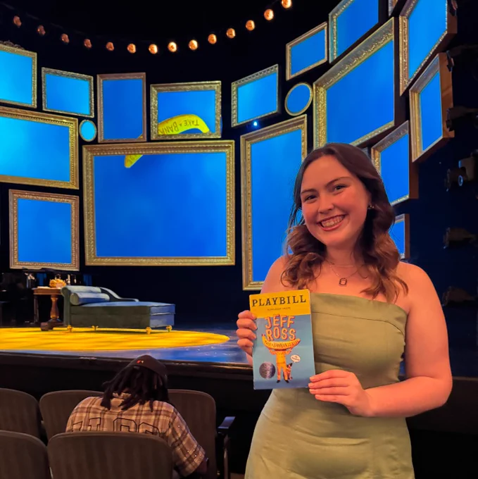 Person holding a Playbill in a theater with multiple empty picture frames on the stage background.