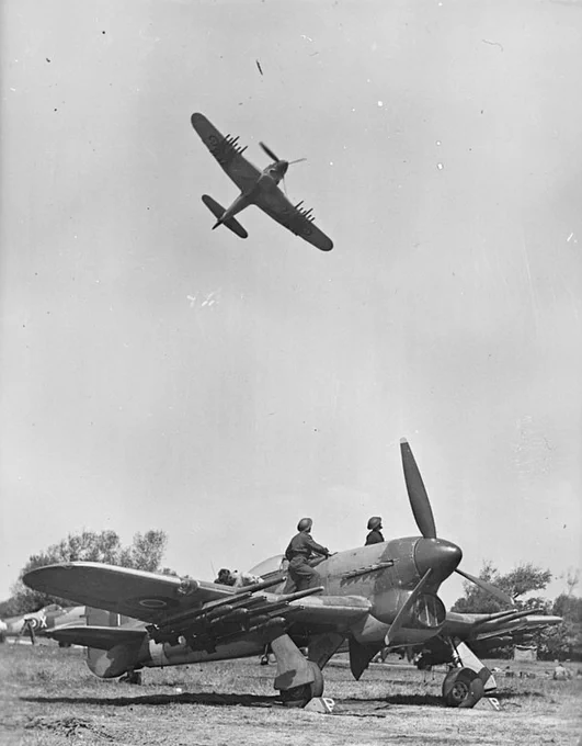 A Typhoon aircraft flies over a grounded Typhoon and its crew.
