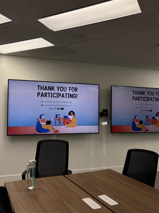 A photo of 2 television screens on the walls of a conference room showing the 'Thank you for participating' slide of the AHA! presentation. 
