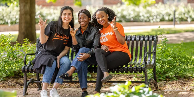 Three individuals seated on a park bench, smiling and gesturing "go pokes" hand sign. 