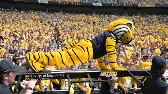 Truman the mascot does pushups on top of a platform being carried by students.