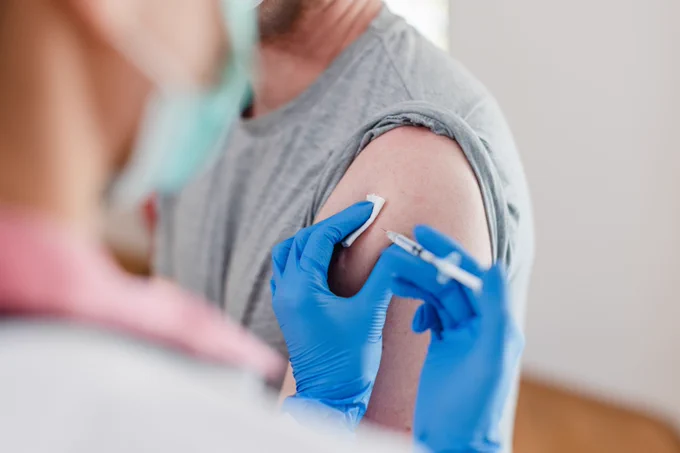 Healthcare worker wearing blue gloves preparing to inject a vaccine into a patient's upper arm 