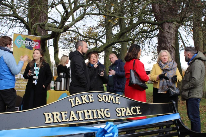 Bench says 'Take Some Breathing Space' with people behind talking