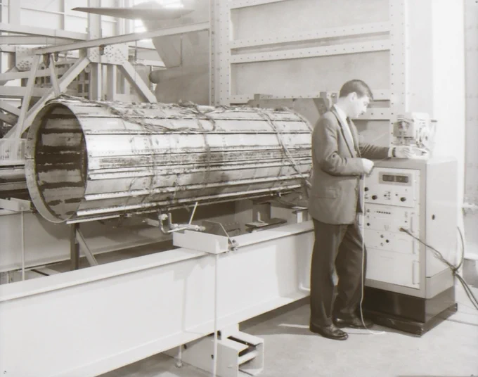 Man in a suit operates a large cylindrical scientific instrument inside a laboratory setting with industrial equipment around.