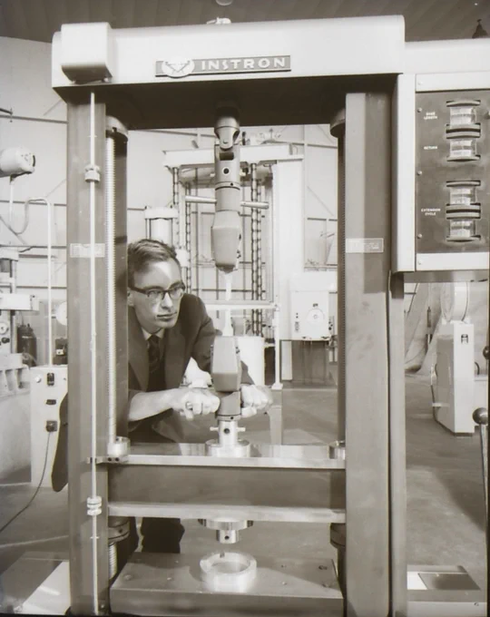 Technician operating an Instron testing machine to measure material strength in a laboratory setting.