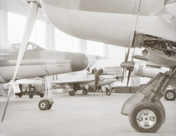 Close-up view of vintage aircraft landing gear and propellers inside a spacious hangar with other planes in the background.