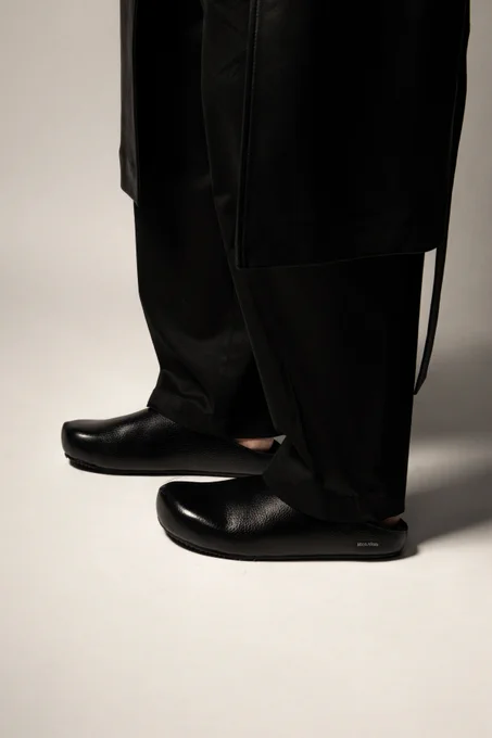 Editorial closeup of some black leather mules, with a shearling lining. Styled with a wide leg trouser.