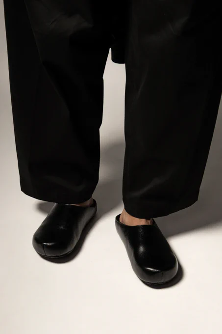 Editorial closeup of some black leather mules, with a shearling lining. Styled with a wide leg trouser.