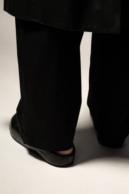 Editorial closeup of some black leather mules, with a shearling lining. Styled with a wide leg trouser.