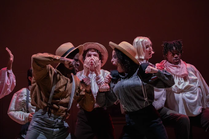 A dynamic theatrical performance featuring actors portraying an intense and expressive scene on a warmly lit stage.