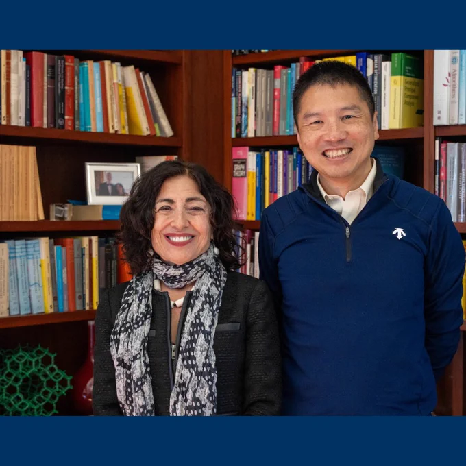Jennifer Chayes and Hao Zhang stand and smile in front of books in a wooden bookshelf.