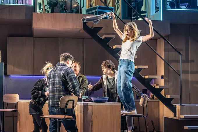 A photo showing a scene on stage where a perfect loving family dance around a kitchen unit together 